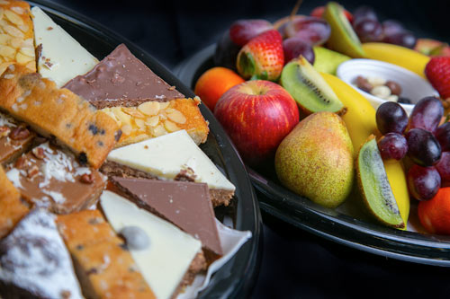 Plated selection of cakes and tray bakes alongside a plate of fruit segments