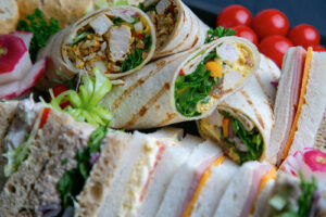 Chicken salad wraps on a tray with assorted sandwiches around them